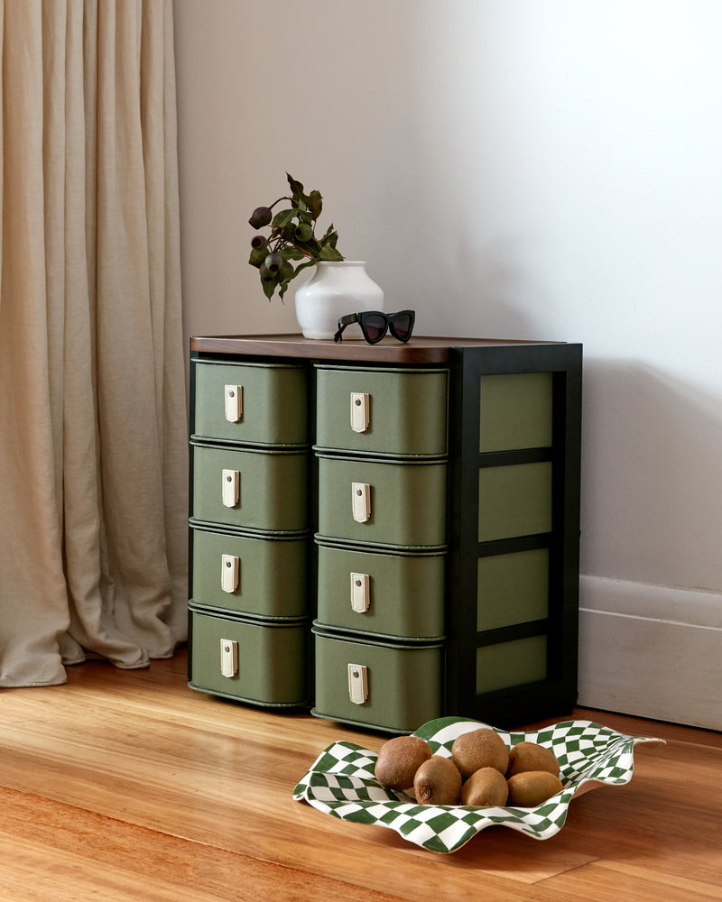 Green storage cabinet with six drawers and wooden top, paired with a decorative dish and sunglasses.