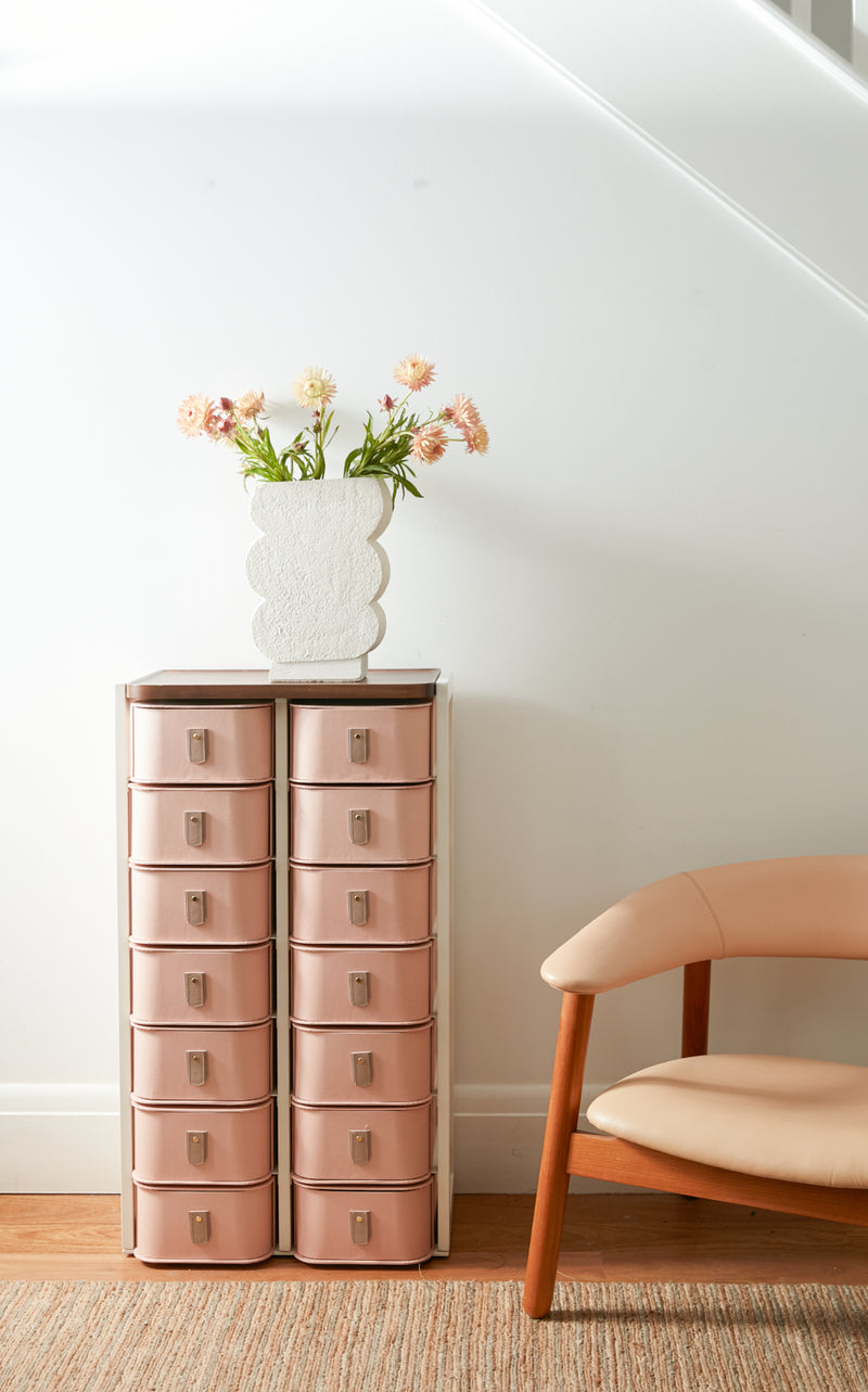 Light pink storage drawers with wooden top and decorative vase on minimalist side table