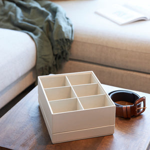 Brown leather belt next to a beige organizer with six compartments on a wooden table.