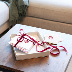 Gift box with red ribbon and wax seal, containing assorted stationery and decorative envelopes from SAGITINE.